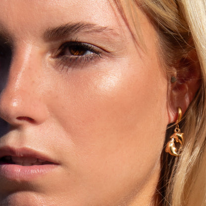 Gold dolphin earrings on ear
